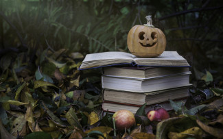秋天的户外场景，树叶散落的草地上，地上有苹果，一堆书，书上面有一个小南瓜灯